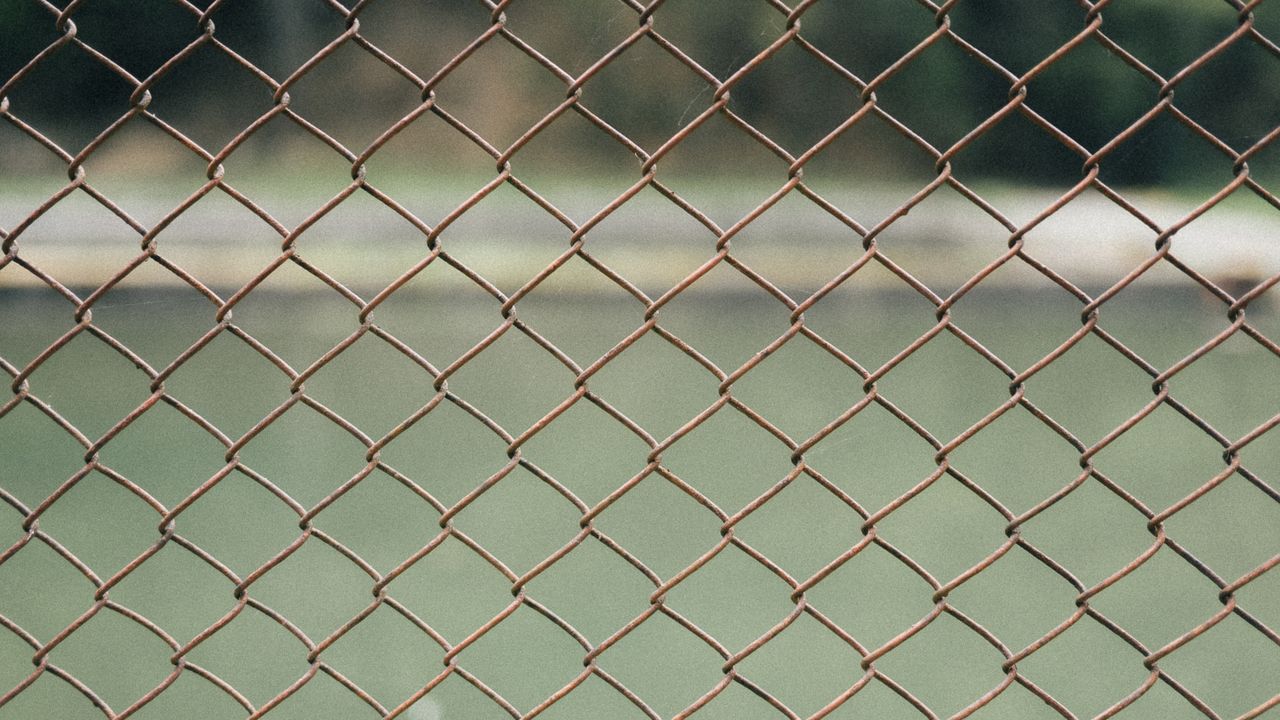Close-up view of a rusty chain-link fence with blurred background, outdoors.