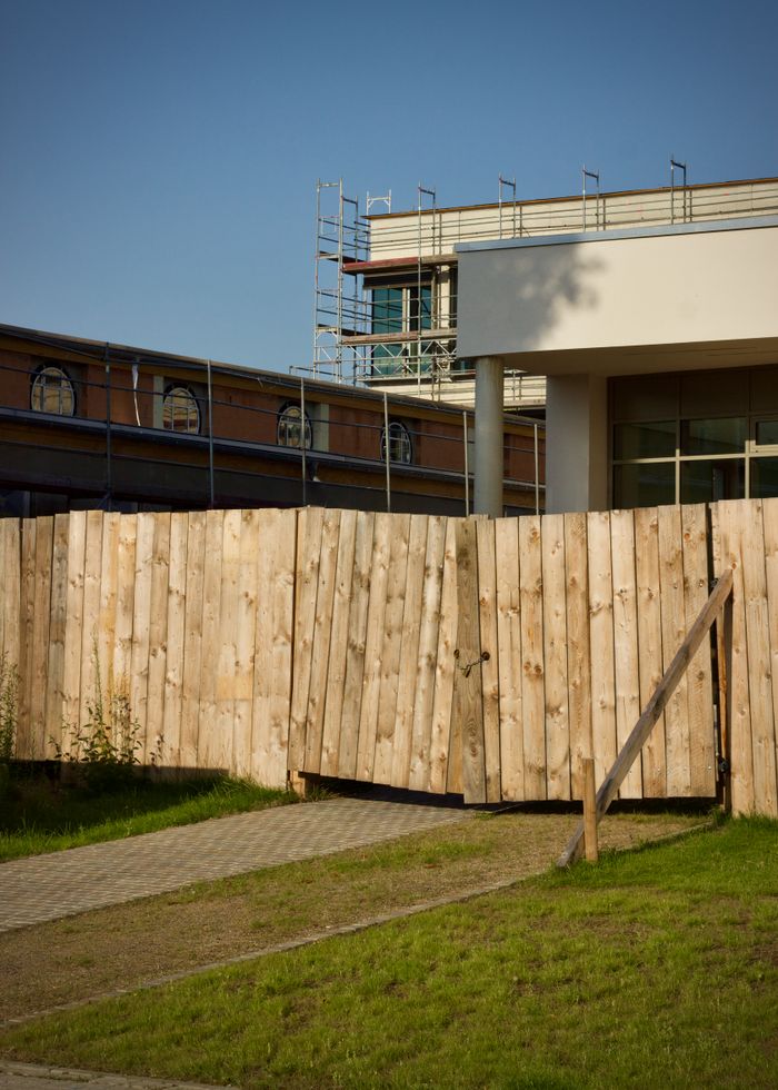 View of a construction site with wooden fence, scaffolding, and modern building structure.